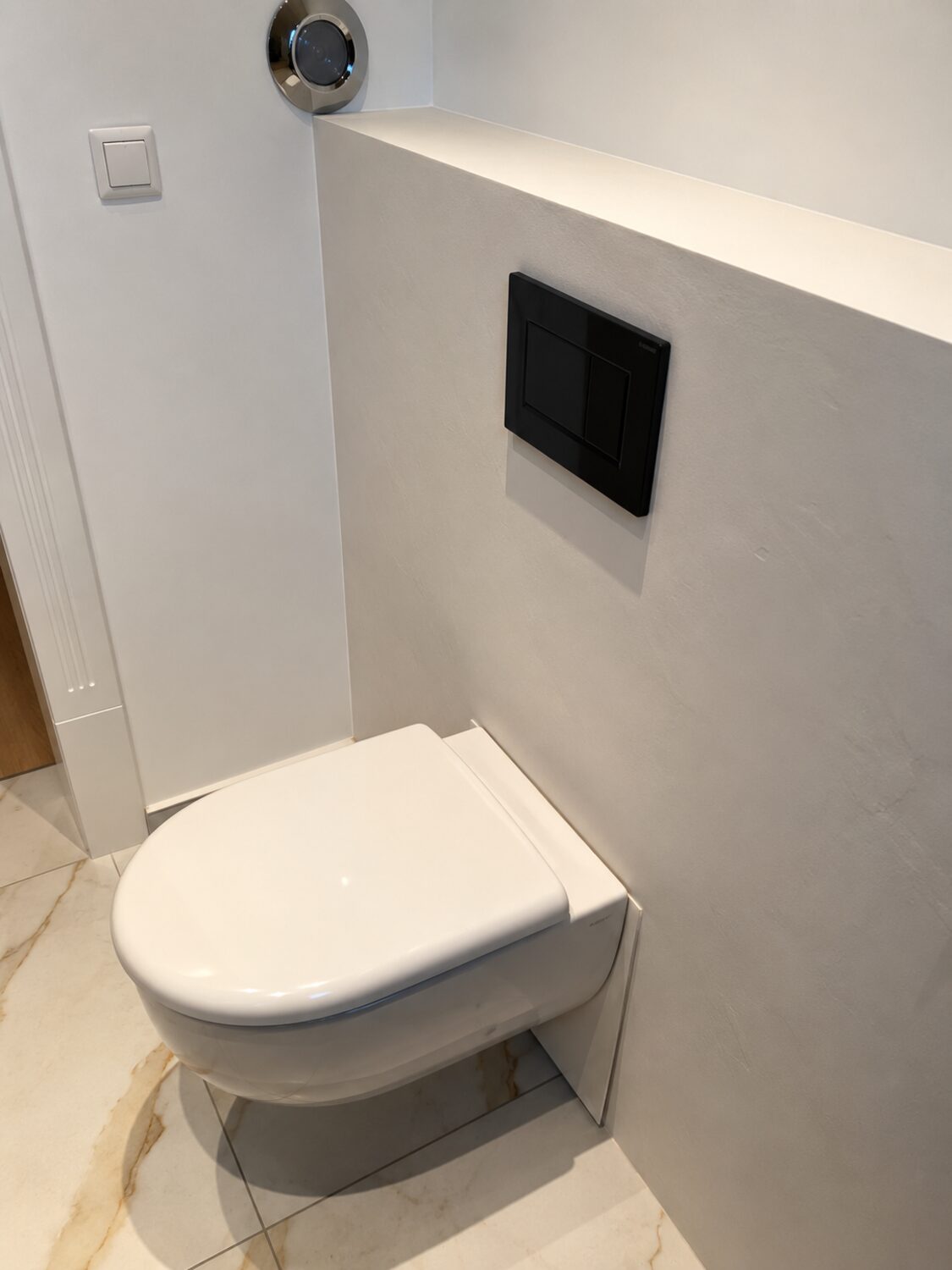 Vorwandinstallation mit Mikrozement beschichtet, wandhängendes WC und schwarze Betätigungsplatte