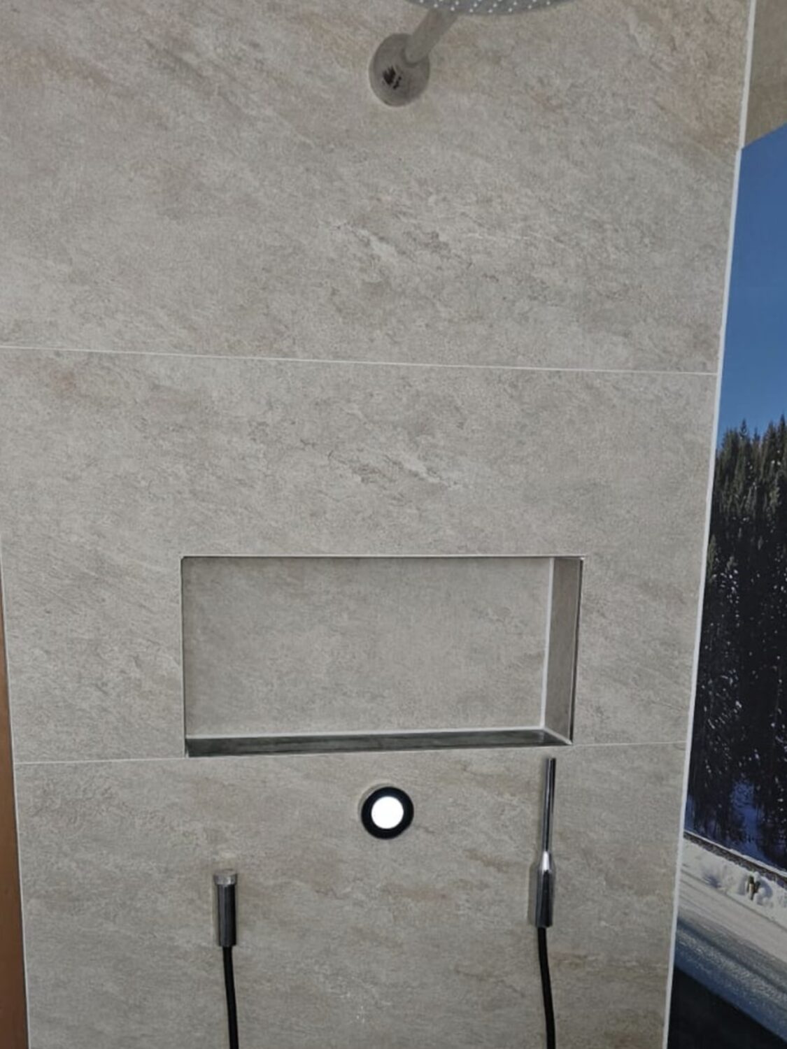 Dusche mit Regenbrause, Handbrause, Wandnische, Bedienknopf mit Leuchtring und Duschrinne, Wände in heller Steinoptik, daneben eine Fototapete mit Bergsee