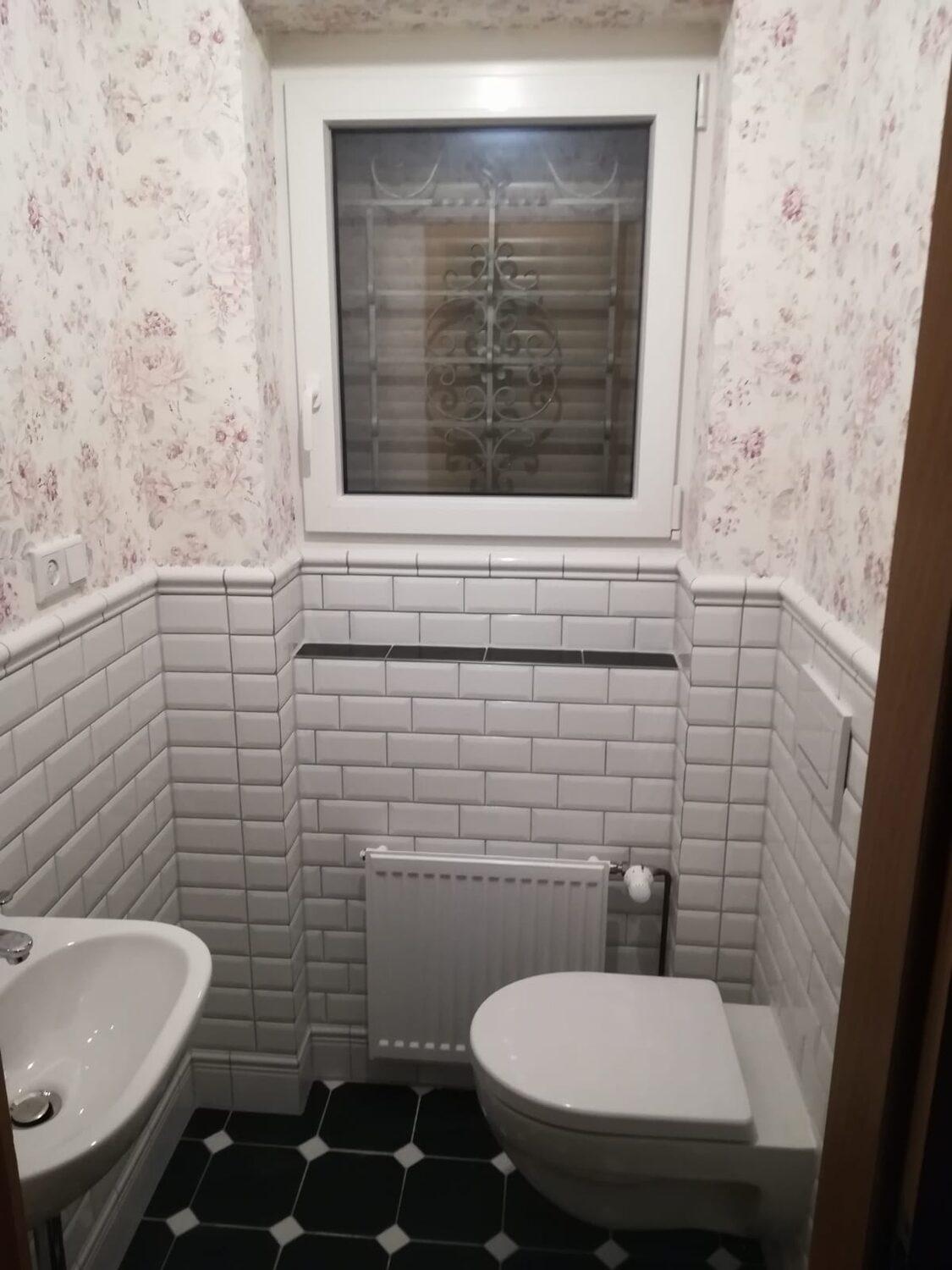 Gäste-WC mit weißen Subway-Fliesen als halbhoher Sockel, darüber florale Tapete in Rosé und Grau, schwarz-weißer Oktogon-Boden